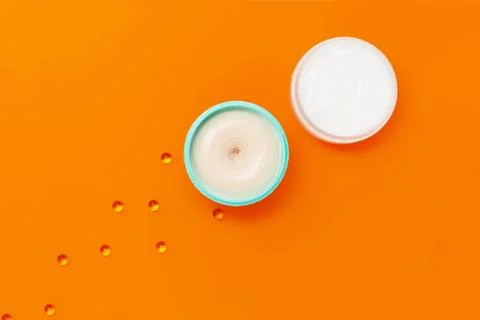 Two jars with different creams on an orange background next to which are caps Stock Photos