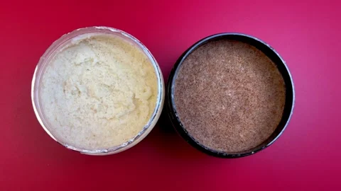Two jars of exfoliating scrubs, one creamy and one granular, placed on a vibrant Stock Footage 321739928