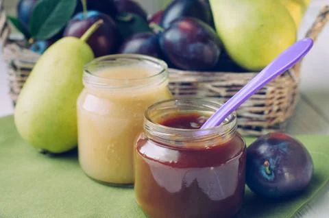 Two jars with prune and pear puree on the table near fresh fruits Stock Photos