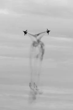 Two jets in V-formation create dynamic smoke trails against cloudy sky during Stock Photos