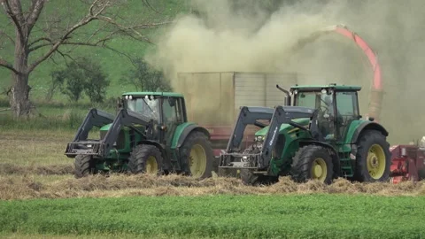 Two John Deere tractors are harvesting dry hay in a meadow and dusting Stock Footage 158499885