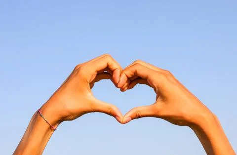 Two joined hands forming the shape of a heart and the blue sky 库存照片