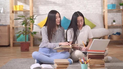 Two joyful young asian students are happy sitting on the floor with textbooks Stock Footage 125802921