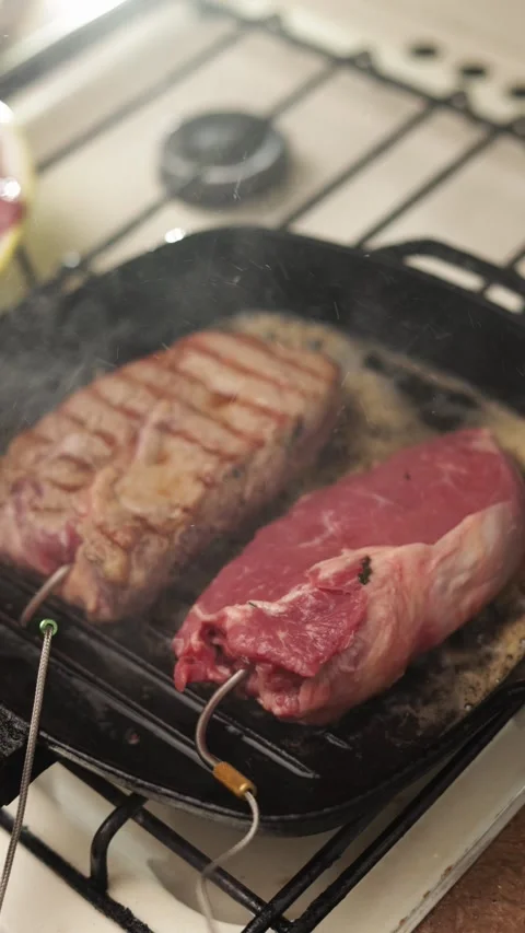 Two juicy steaks searing in a hot cast iron grill pan with steam rising Vidéo 340563285