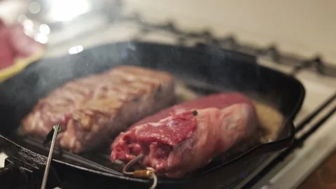 Two juicy steaks sizzling in a cast iron pan on a gas stove Stock Footage 340563284