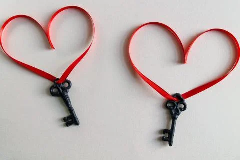 Two keys with a red ribbon in the shape of a heart on a light surface Stock Photos