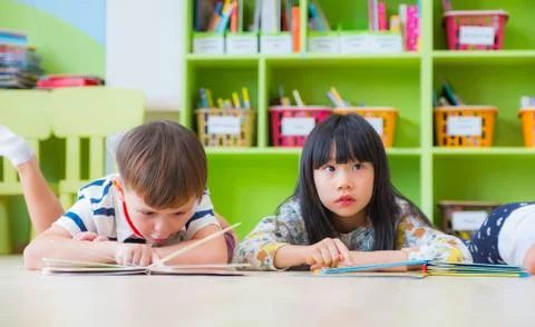 Two kid lay down on floor and reading tale book in preschool library,Kinderga Stock Photos