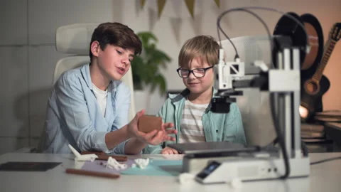 Two kids are actively discussing the parts they just printed on the 3D printer Stock Footage 335375711
