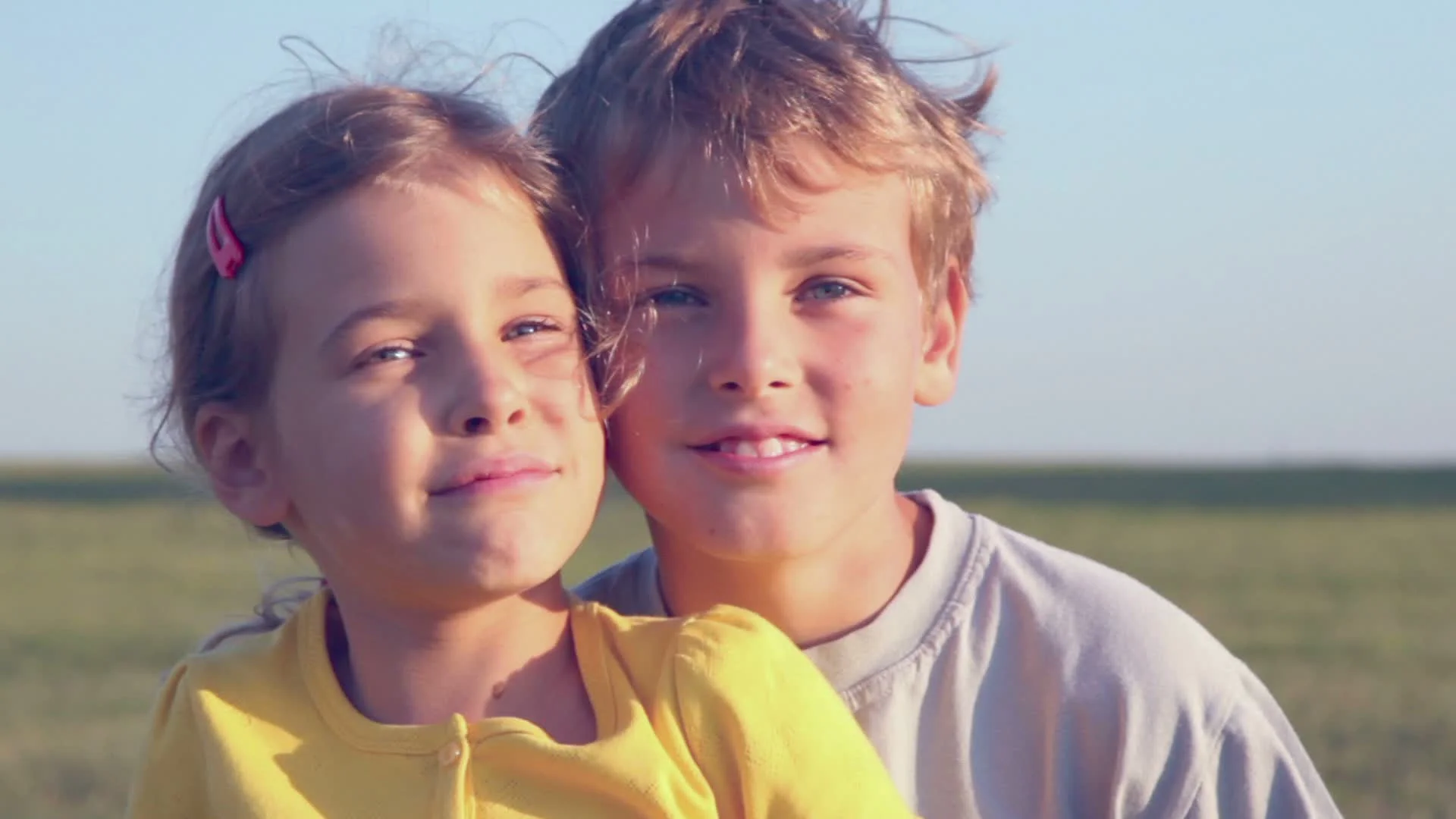 Two kids boy and little girl sit close together on grass hill