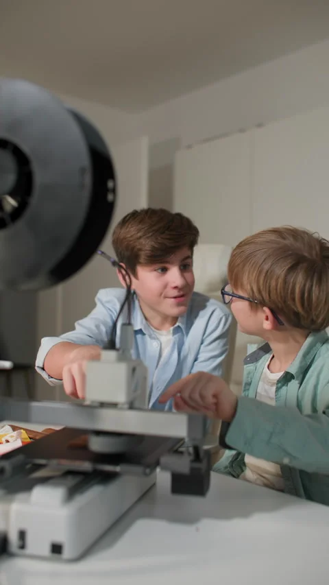 Two kids controlling work of a 3D printer. And they are both happy they job Stock Footage 335390887