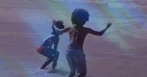 Two kids crouching, hopping as small waves sparking play in travel clip with Stock Footage 330917094
