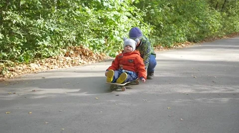 Two kids funniest play while sitting on the skateboard in the Park Vídeo Stock 68206197