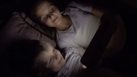 Two kids lying down on the sofa and watch funny movie on tablet pc at night. Stock Footage 72371058