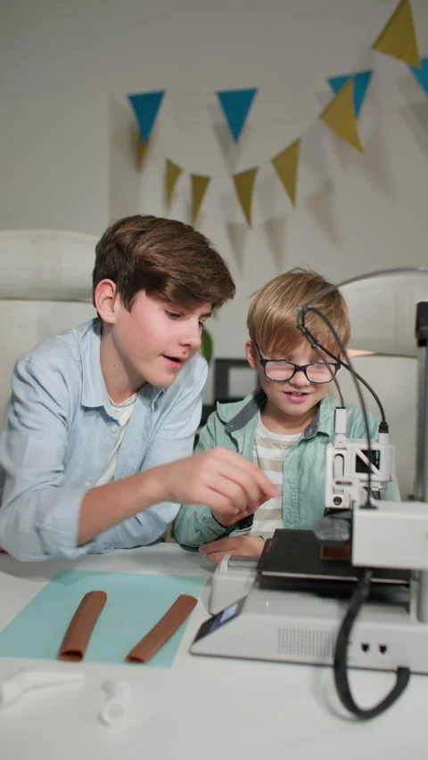 Two kids observe, chatting the operation of a 3D printer. They play with it Stock Footage 335391758