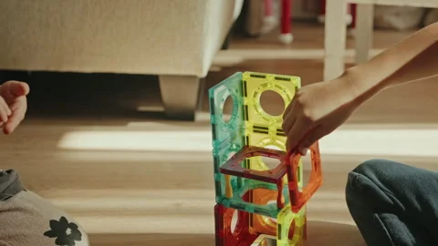 Two kids playing with multi-colored magnetic constructors, building a tower Stock Footage 254651333
