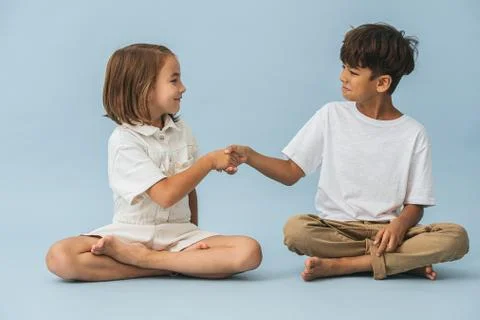 Two kids of roughly the same age sitting on the floor cross-legged Stock Photos