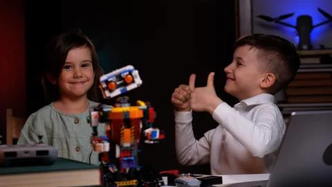Two kids showing thumbs up while building robot from plastic parts Foto stock