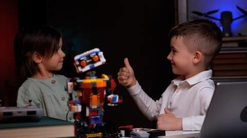 Two kids showing thumbs up while building robot from plastic bricks 스톡 사진
