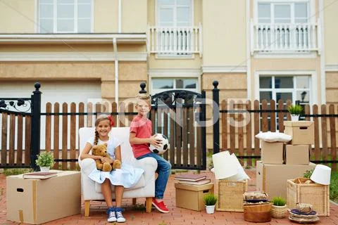 Two kids sitting in armchair in the front yard with packed things near by Stock Photos