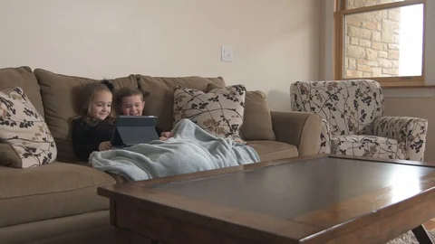 Two kids sitting on couch watching a show from their tablet Stock Footage 85488684