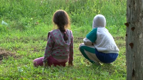 Two kids sitting on green grass holding hands and play, back to camera Stock Footage 63395749