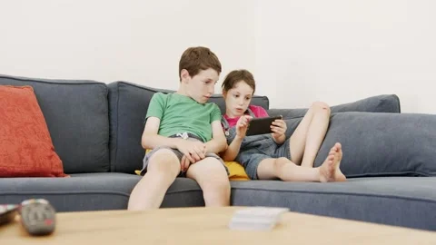 Two kids sitting on a large sofa at home, using a mobile phone Stock Footage 133967181
