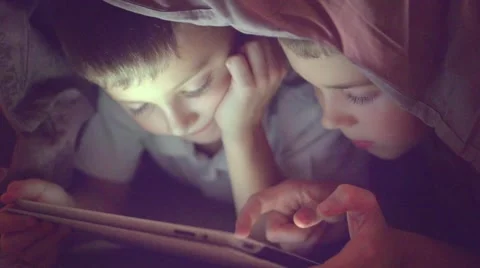 Two kids using tablet pc under blanket at night. Video stock 67357887