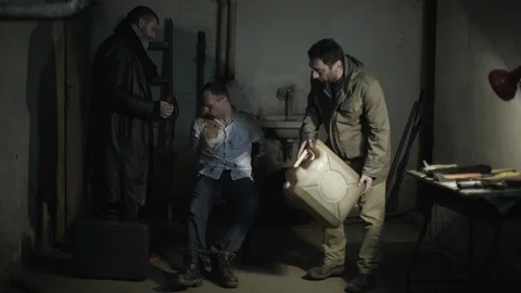 Two killers spilling gasoline on tied victim and burning kidnapped male hostage. Stock Footage 86320643