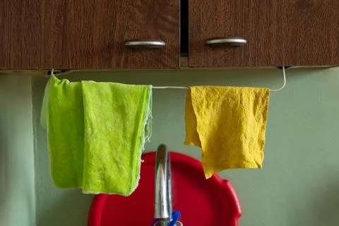 Two kitchen rags, green and yellow, hang on a rope above the sink under a woo Stock Photos