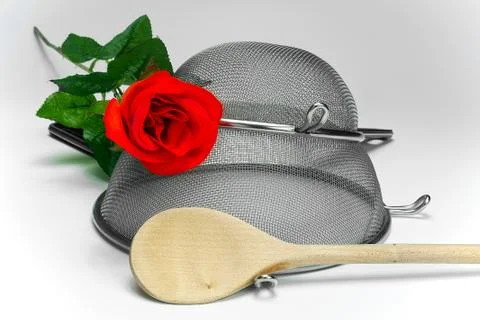 Two kitchen sieves with red rode and wooden spoon on black background, decora Stock Photos