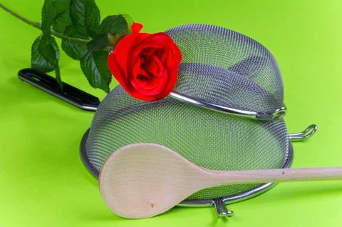 Two kitchen sieves with red rose, wooden spoon on a green background, decorat 스톡 사진