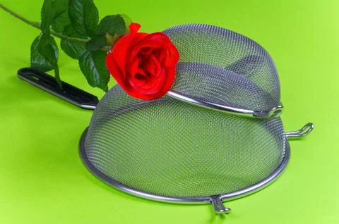 Two kitchen sieves with red rose and wooden spoon on green background, decora Stock Photos