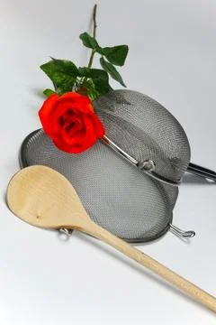Two kitchen sieves with red rose and wooden spoon on white background, decora Stock Photos