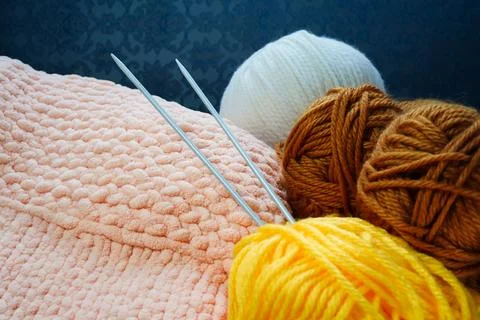 Two knitting needles stick out from a ball of yarn and a piece of knitted goods. Stock Photos