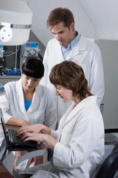 Two lab technicians watching as a third tech types notes on a laptop Foto stock