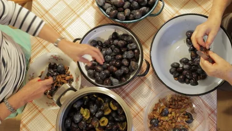 Two ladies pitting and sorting plums on a kitchen table Stock Footage 140644533