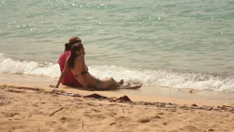 Two ladies sitting at the edge of the ocean with water splashing on their legs Stock Footage