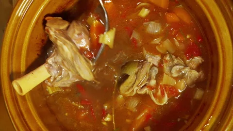 Two lamb shanks being stirred in a cooking pot with vegetables. Stock Footage 246634965