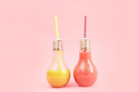 Two lamp- shaped jars with fruit smoothies isolated on pink background. Stock Photos