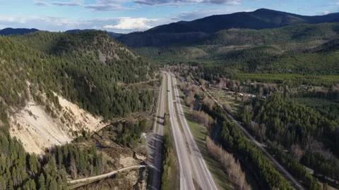 Two-lane highway cuts through dense pine forest and mountain valley near Stock Footage 337692436