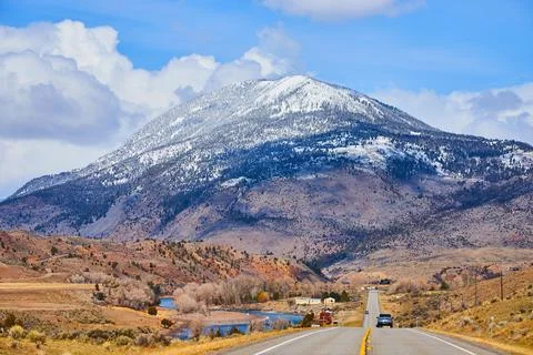 Two-lane paved road in mountains leading towards huge snowy mountain in western Stock-Fotos