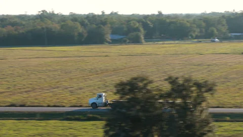 Two lane road through open fields with flatbed truck tractor trailer moving Stock Footage 335254186