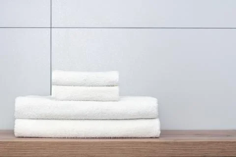 Two large and two small neatly folded white towels lie on a wooden shelf agai Stock Photos