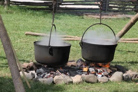 Two large, black , steaming, cooking pots hanging over open outdoor fire. Stock Photos
