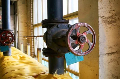 Two large black valves on the heating pipe insulated with a yellow cloth. Stock Photos