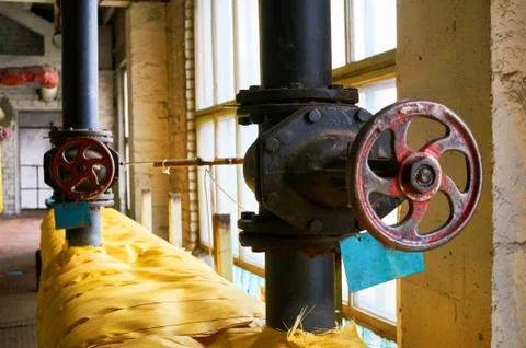 Two large black valves on the heating pipe insulated with a yellow cloth. Stock Photos