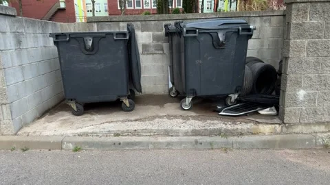 Two large black wheeled garbage bins in concrete block enclosure 動画素材 344041557