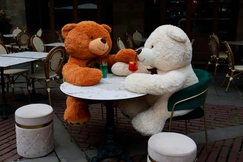 Two large brown and white teddy bears sitting on top of a table, enjoying coc Stock Photos