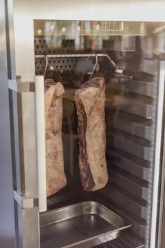 Two large cuts of beef are hung inside a modern refrigerator designed for d.. Stock Photos