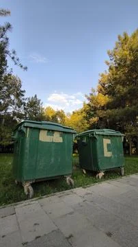 Two large green plastic waste containers on the grass next to a pavement. 库存照片